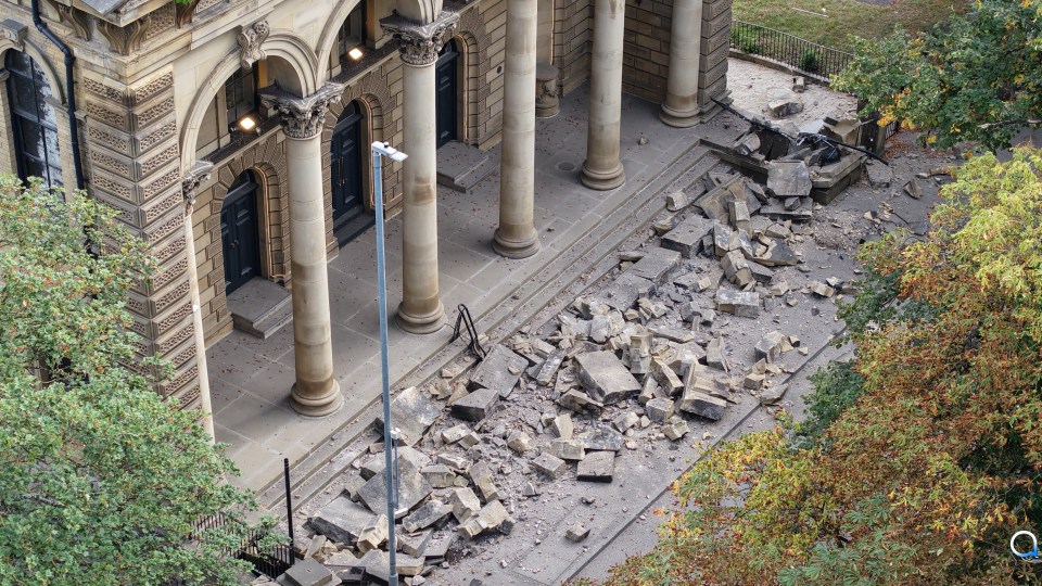 Debris from a collapsed building facade lies on the pavement.