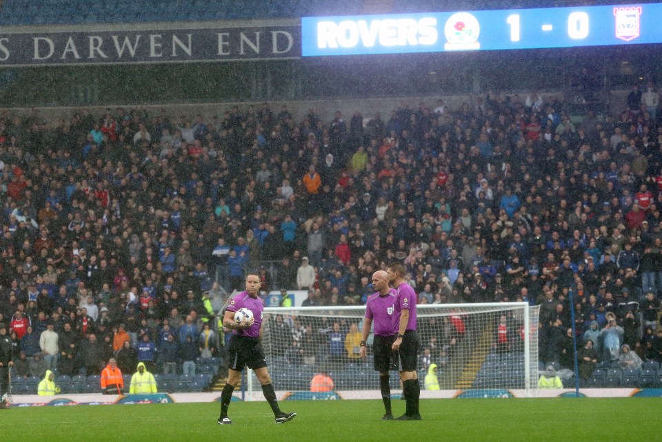 Referee Stephen Martin holding a soccer ball while inspecting a waterlogged pitch during a match between Blackburn Rovers and Ipswich Town.