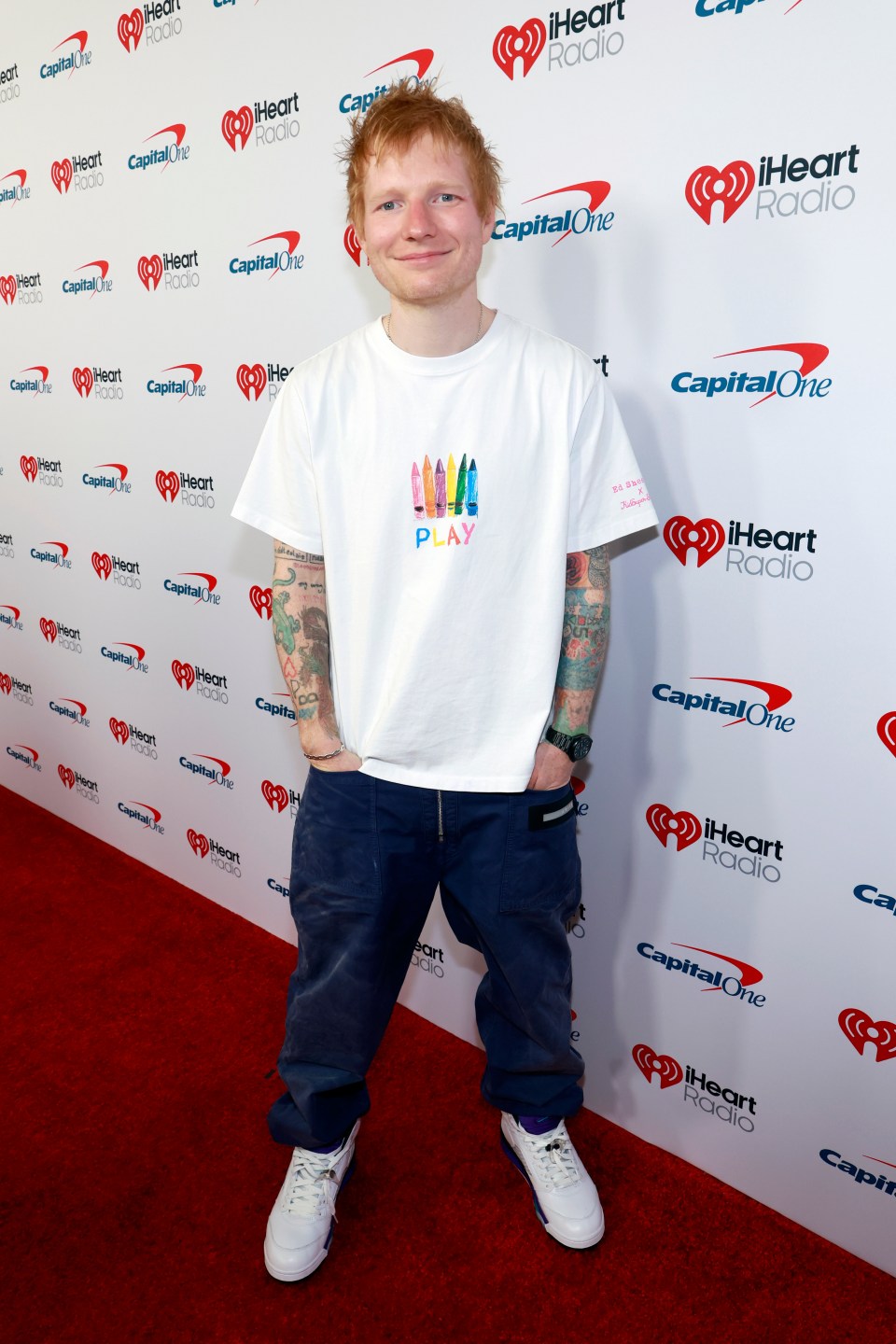 Ed Sheeran on a red carpet in front of a white backdrop with iHeartRadio and Capital One logos.