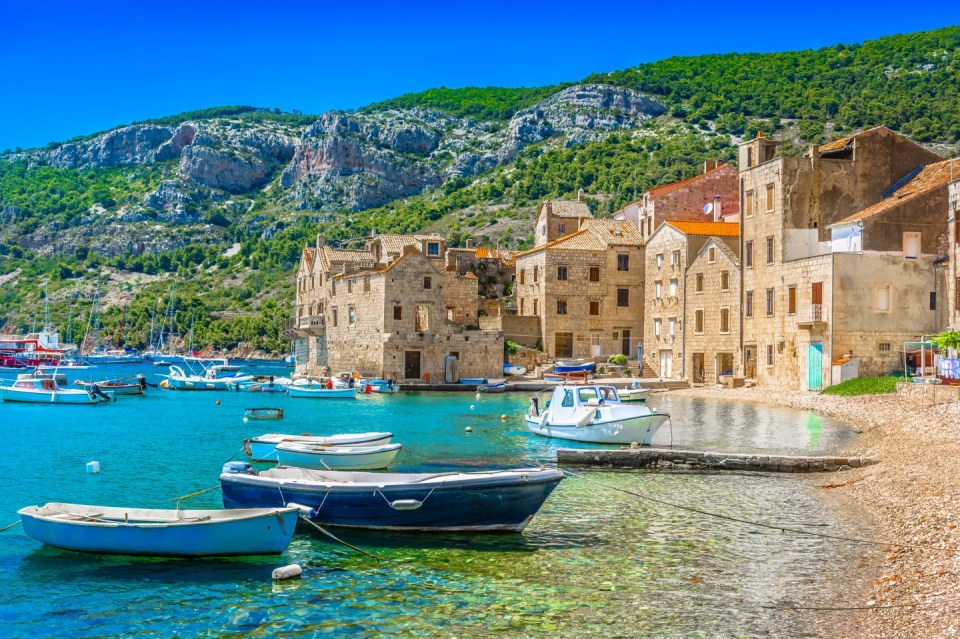 Scenic view of Komiza harbor with boats and stone buildings.