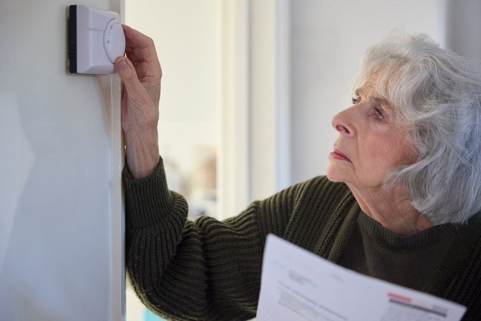 Worried senior woman lowering thermostat while reviewing a bill.