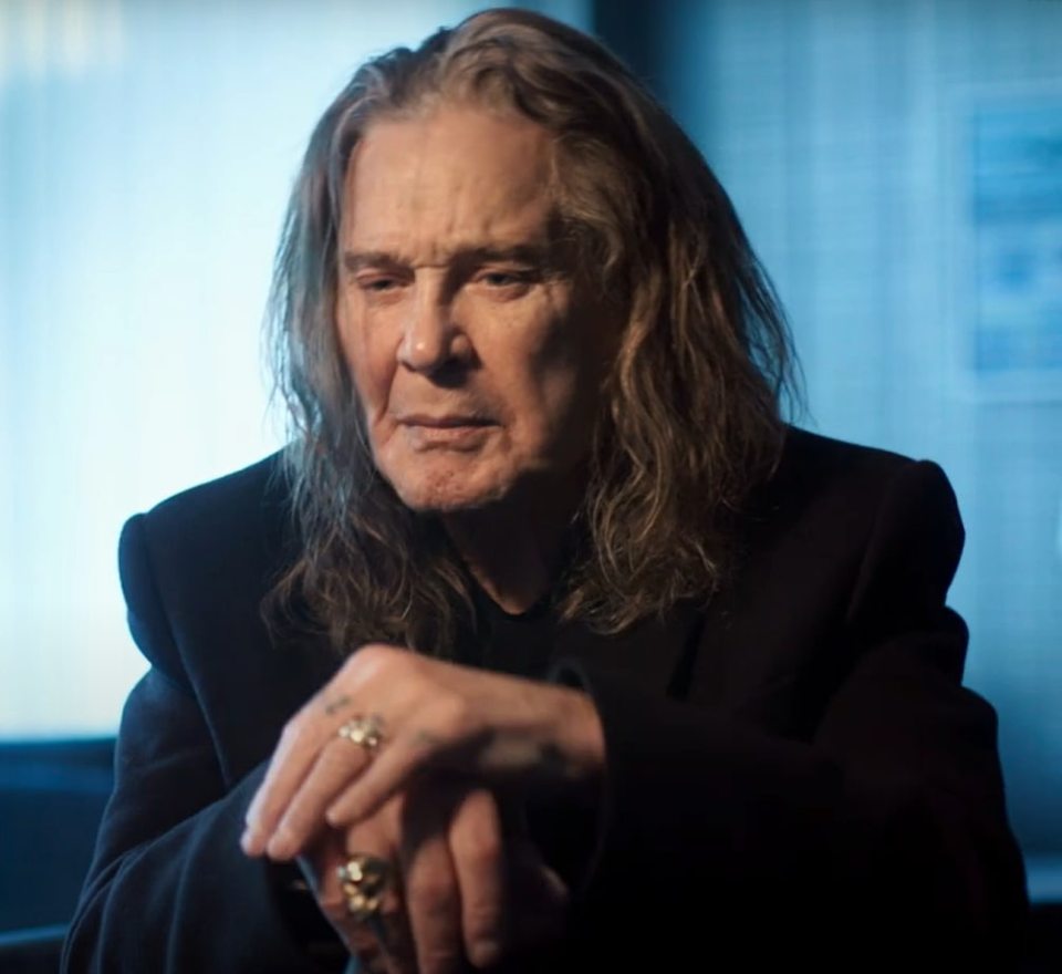 Ozzy Osbourne sitting with his hands clasped, wearing rings.