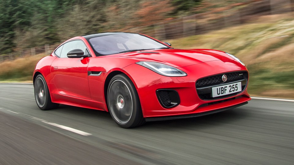 A red 2014-2020 Jaguar F-Type petrol coupe driving on a road.