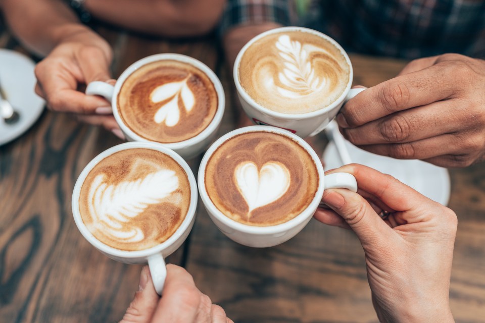Hands of four people holding cappuccino cups with latte art.
