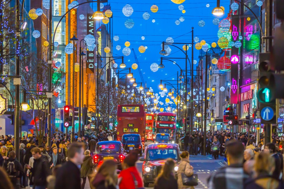 Christmas lights decorate Oxford Street in London with crowded sidewalks, red double-decker buses, and black cabs on the street.