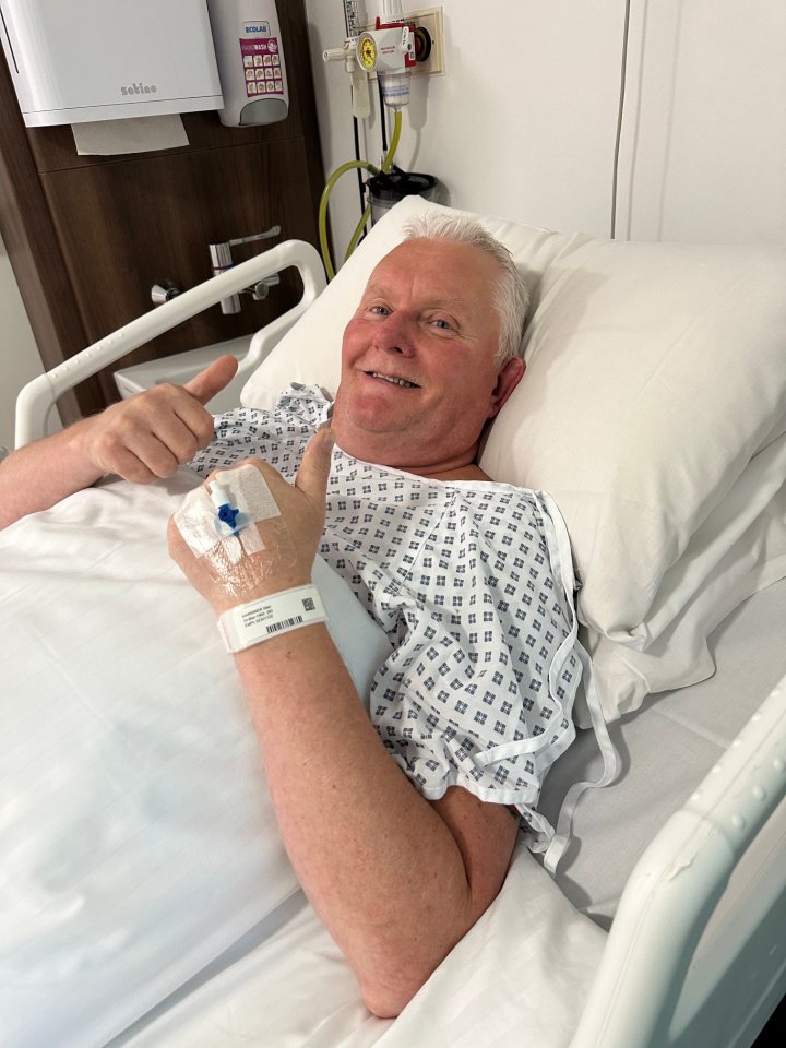 Alan Warriner-Little in a hospital bed, giving two thumbs up.