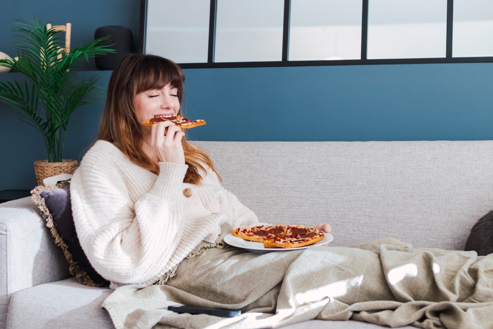 Woman enjoying pizza on sofa at home.