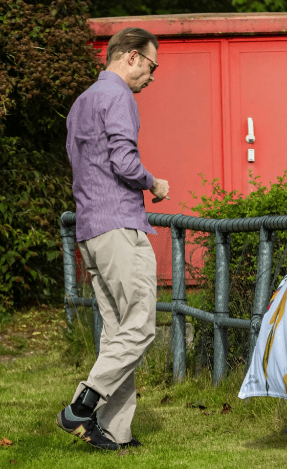 A man in a striped shirt and khaki pants walks with an ankle monitor on his leg.