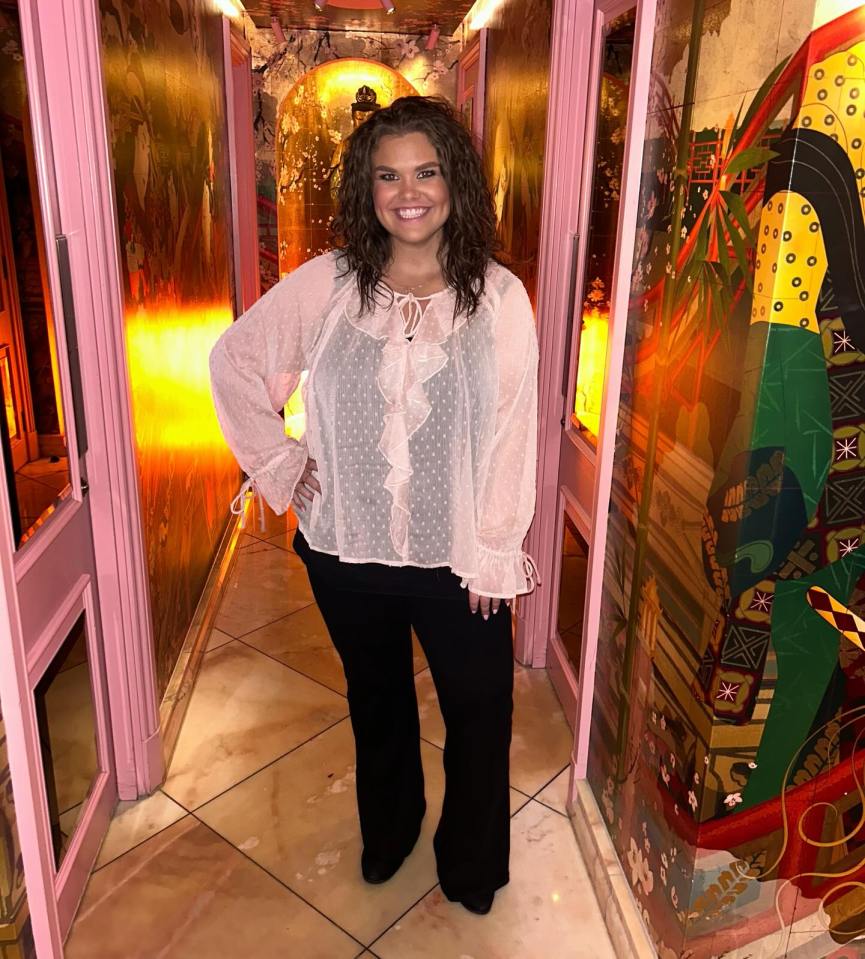 Woman in a pink top and black pants standing in a decorative hallway.