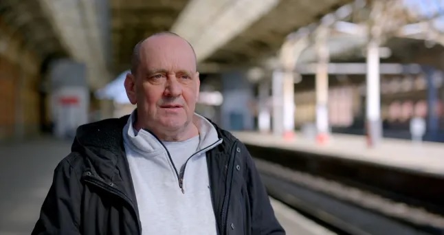 A 58-year-old man, Peter Macdonald, on a train platform, looking overcome with emotion.