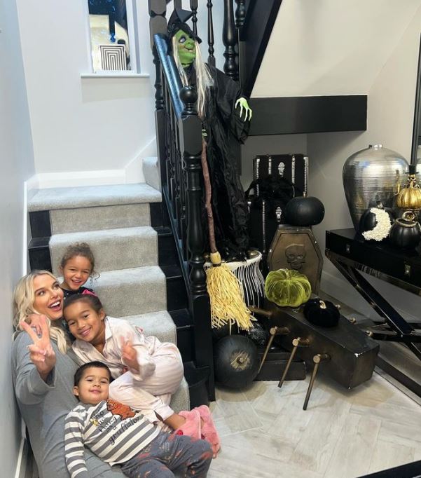 Woman with three children sitting on stairs in front of Halloween decorations.