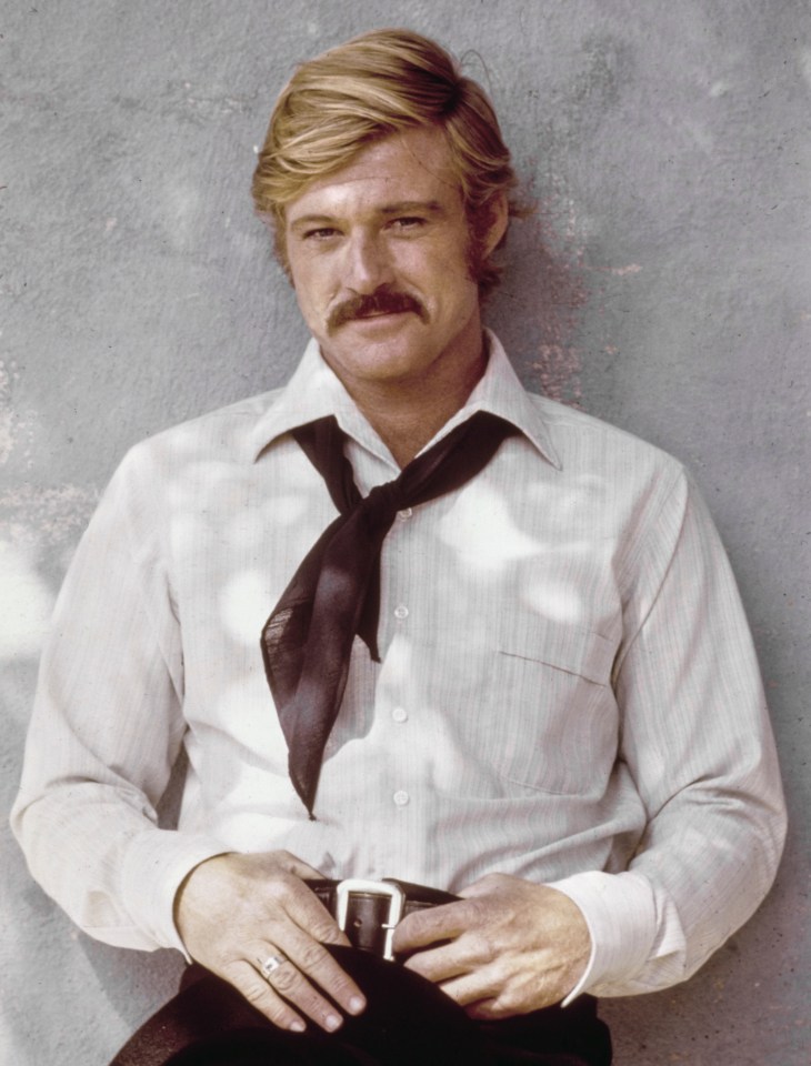 American actor Robert Redford with a mustache, wearing a white shirt and black neckerchief.
