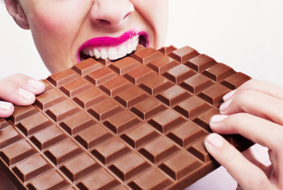 Woman with pink lipstick biting into a large bar of milk chocolate.