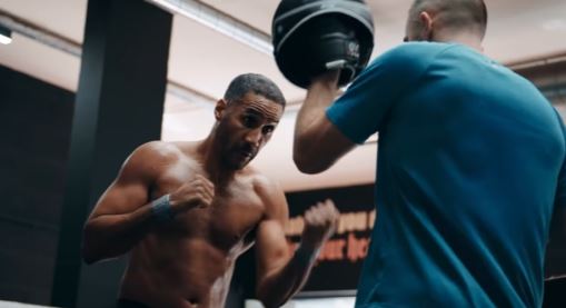 A shirtless boxer training with a pad holder.