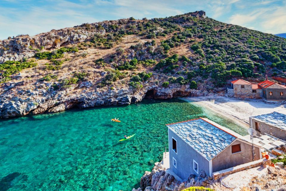 Kayakers in turquoise water near a secluded beach in Evia, Greece.