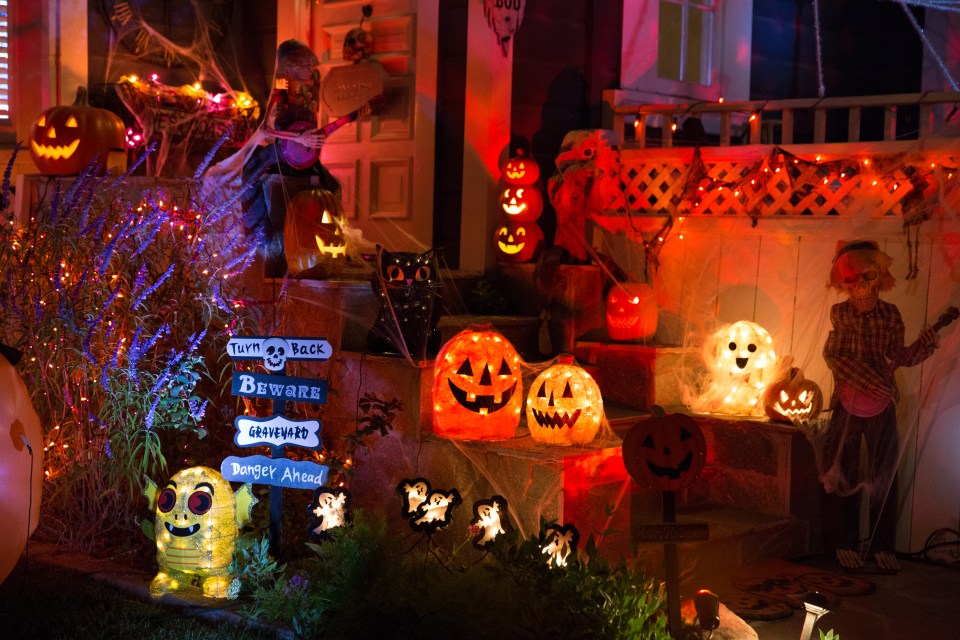 A house decorated for Halloween at night with lit-up pumpkins, skeletons playing instruments, ghosts, and spiderwebs.