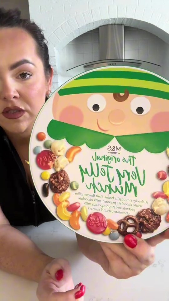 A woman holding a round M&S Munch Box filled with snacks.