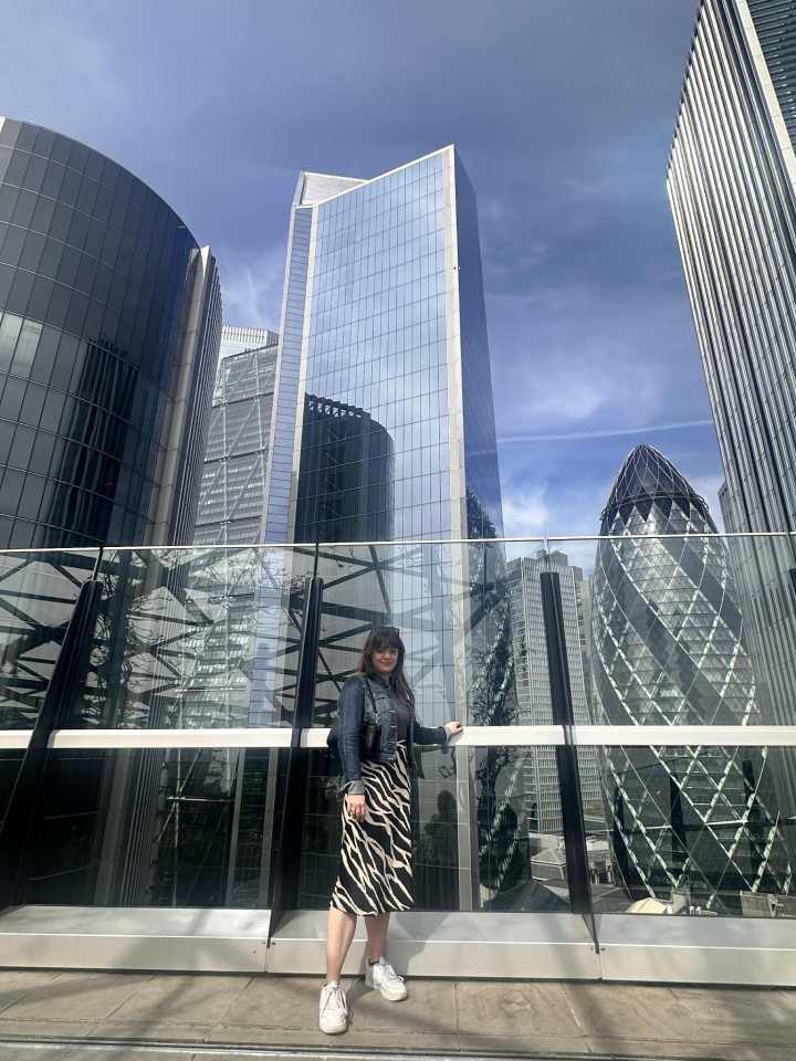 Woman in zebra-print skirt standing on a bridge overlooking London skyscrapers.