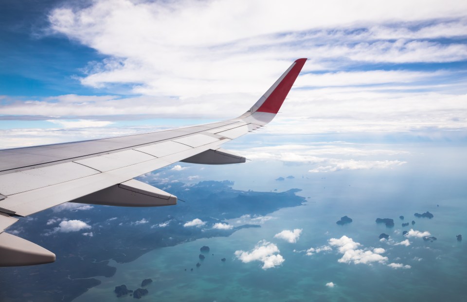 Airplane wing over coastal islands and ocean.