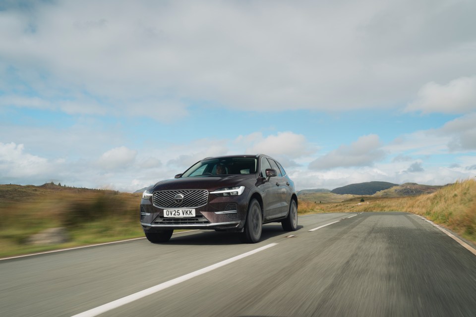 A burgundy Volvo XC60 driving on a road with hills and fields in the background.