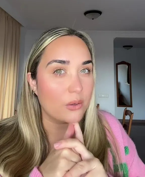 A woman with blonde hair and green eyes wearing a pink sweater.