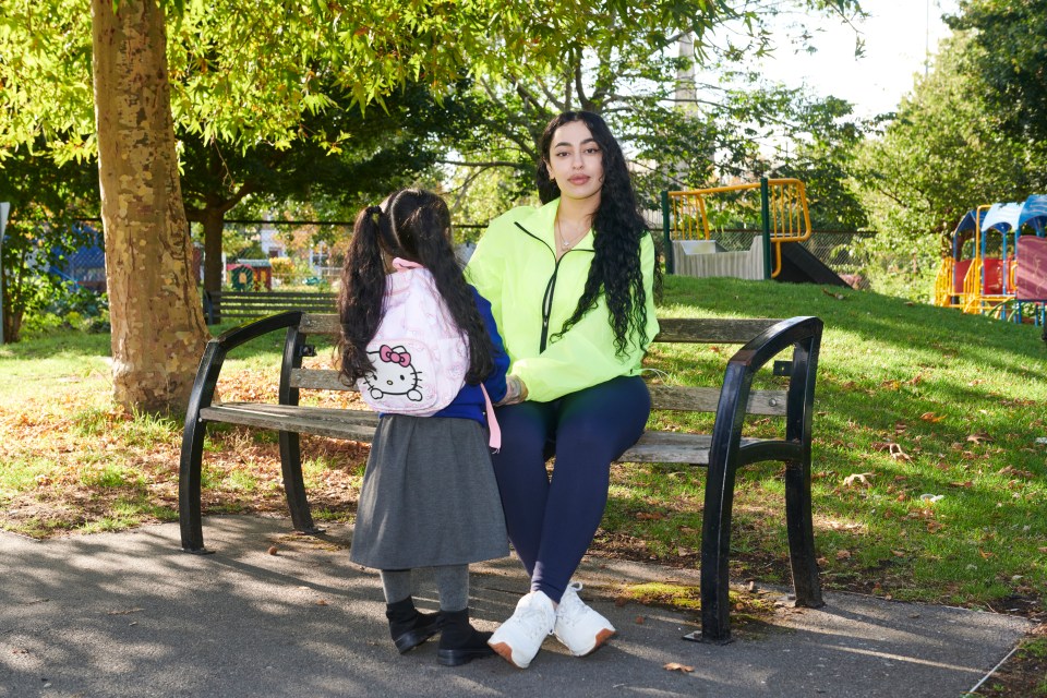 A mother and her young daughter sit on a park bench.