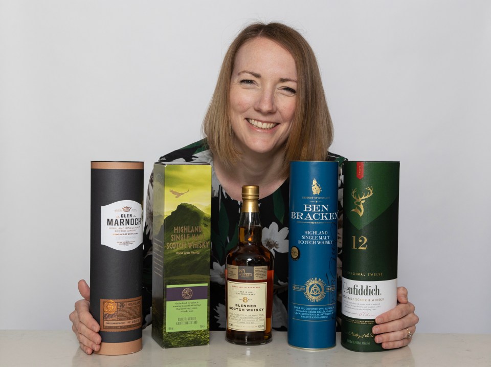 Woman smiling and holding various bottles and boxes of Scotch whisky.