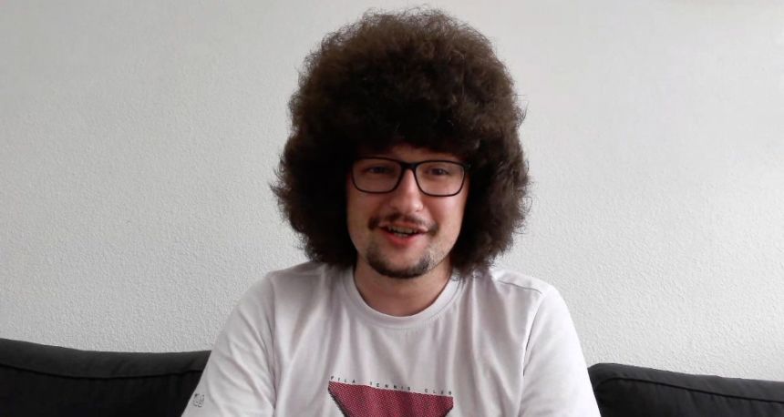 Man with an afro, glasses, and a mustache wearing a white t-shirt.