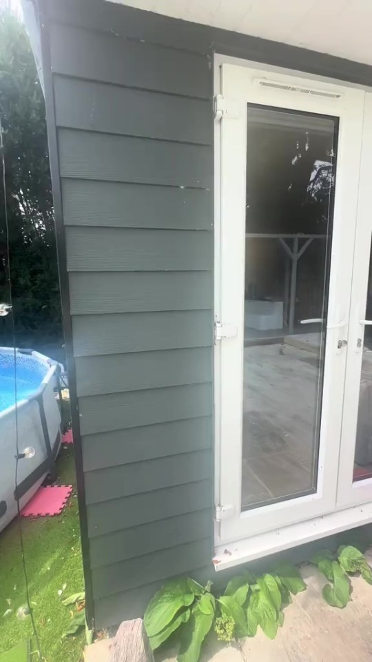 Side of an annexe with dark green siding and white French doors, next to an above-ground pool.