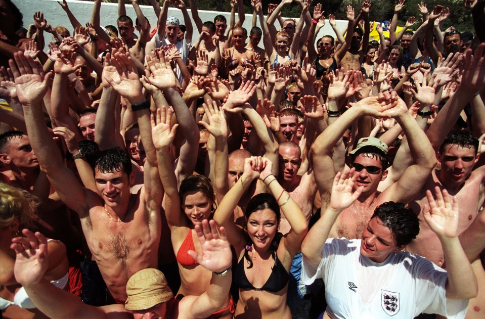 Large group of young people at a pool party, raising their hands.