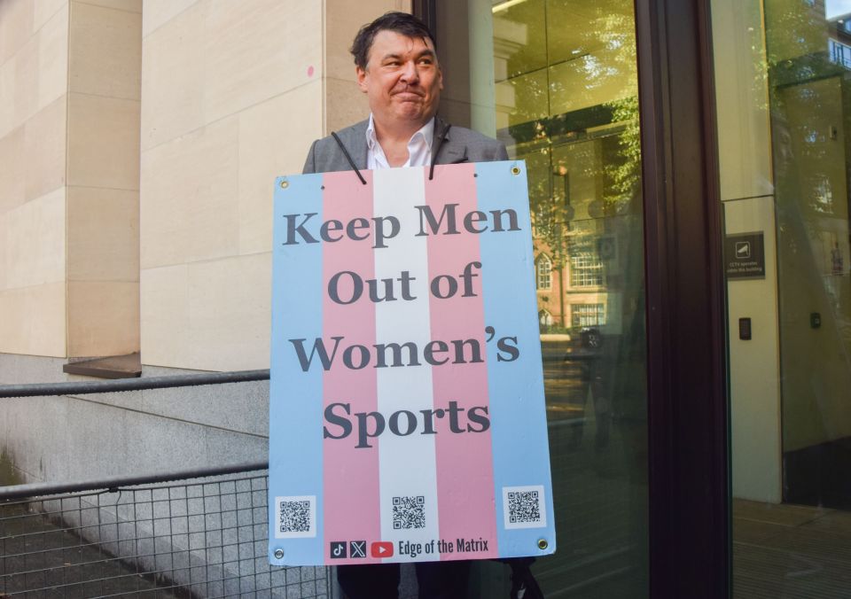 Graham Linehan holding a sign that reads "Keep Men Out of Women's Sports."