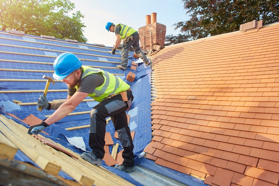 Two roofers install terracotta tiles on a roof.