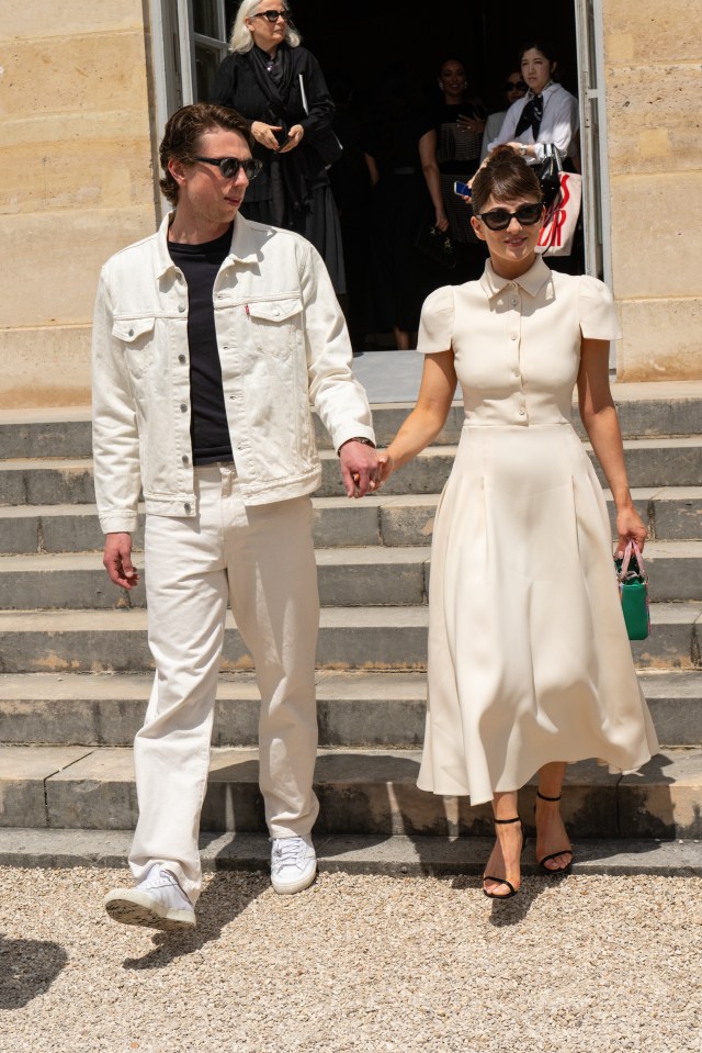 Jamie Bogyo in a cream denim jacket and pants, and Marisa Abela in a cream midi dress, holding hands while leaving the Dior show.