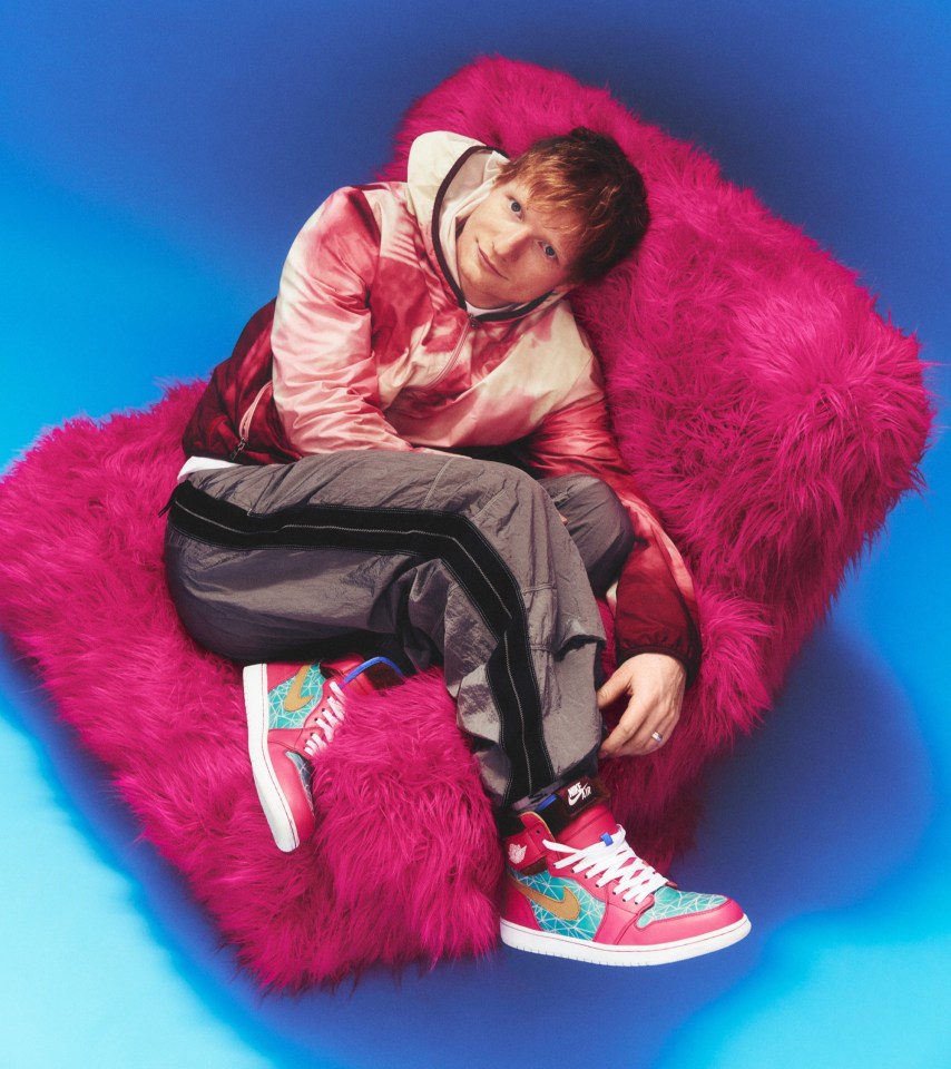 Ed Sheeran sitting on a pink fluffy chair against a blue background.