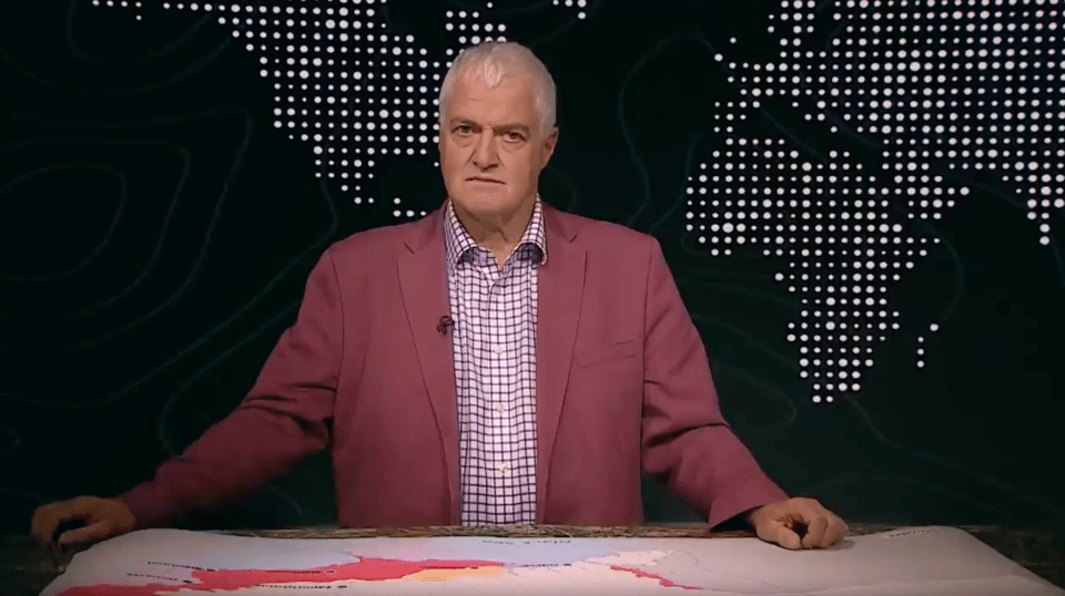 Man in a pink jacket presenting in front of a world map.