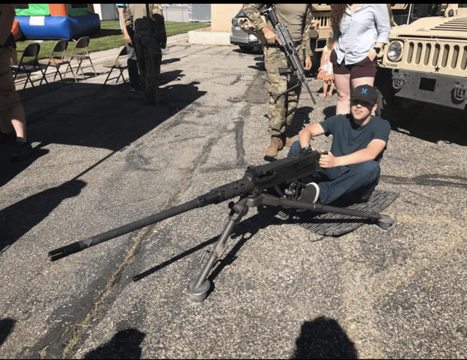 A young man sits next to a machine gun.