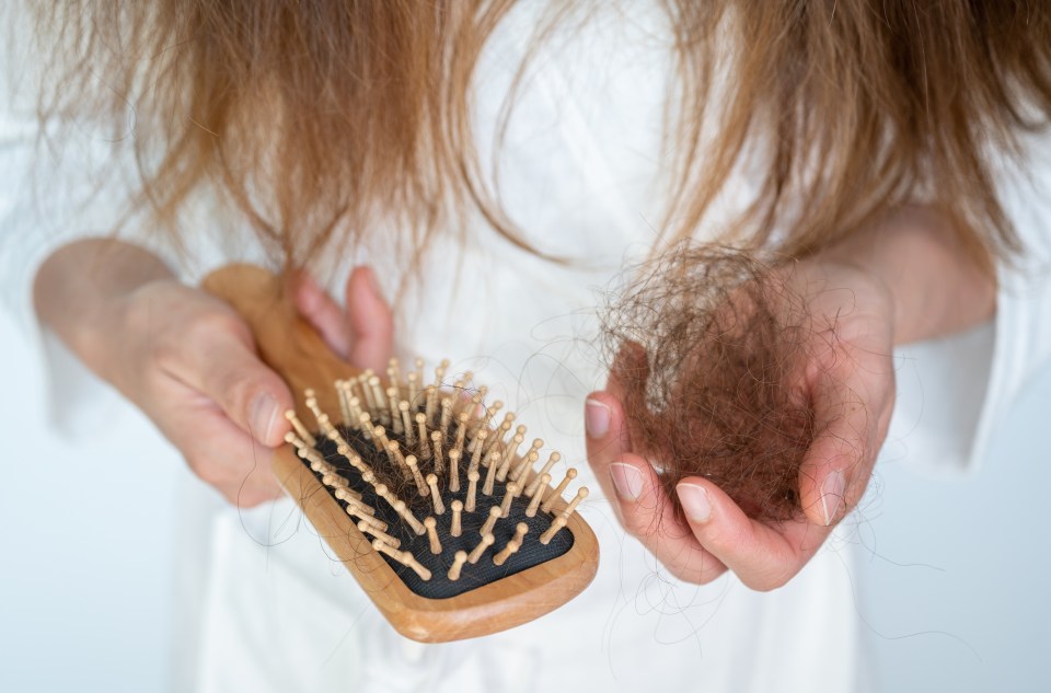 Woman holding a brush and a clump of hair, showing hair loss.