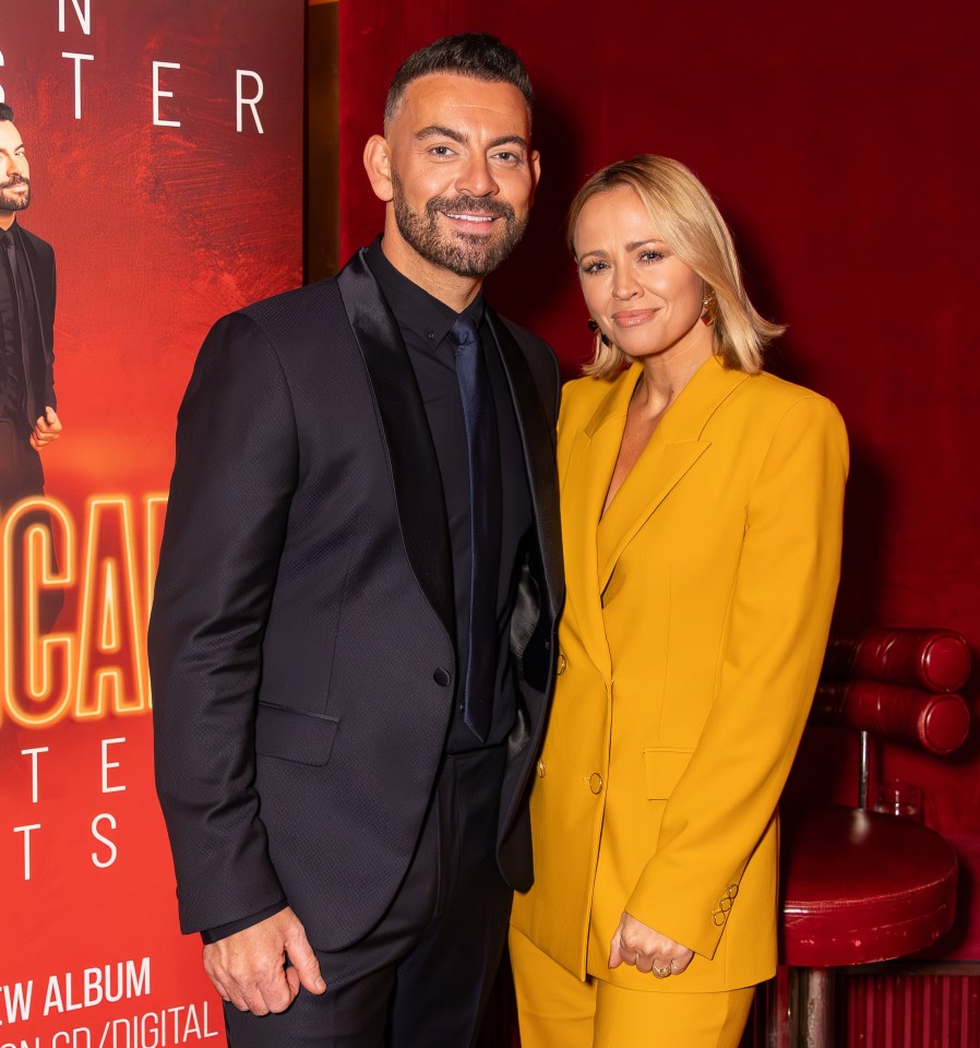 Ben Forster and a woman stand next to a red banner advertising Ben Forster's new album, "Musical Greatest Hits."