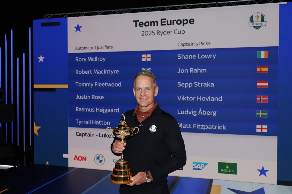 Luke Donald, 2025 Ryder Cup Team Europe captain, holding the Ryder Cup trophy.  The team roster is visible behind him.