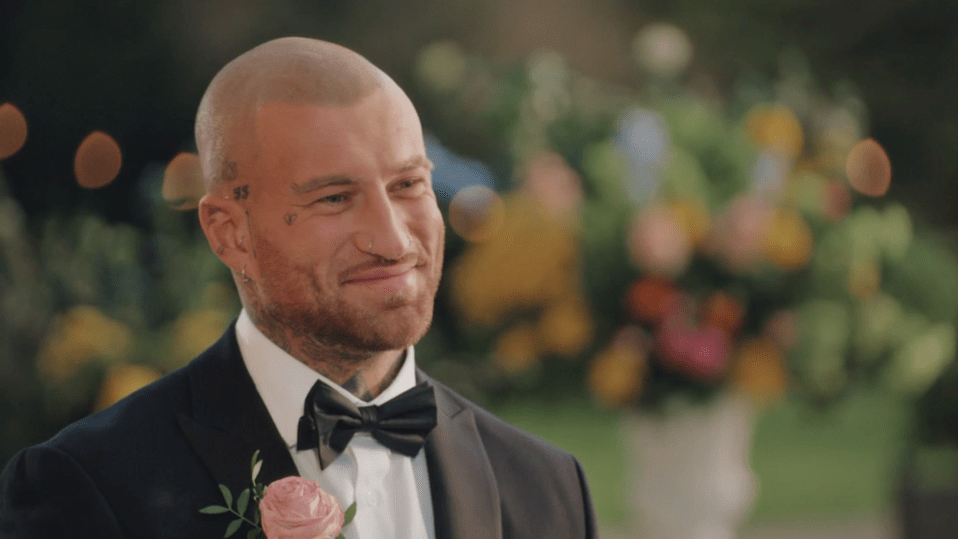 A smiling man in a tuxedo with a pink boutonnière.