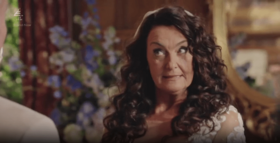 Woman with curly brown hair looking up and to the right, wearing a wedding dress with white lace sleeves.