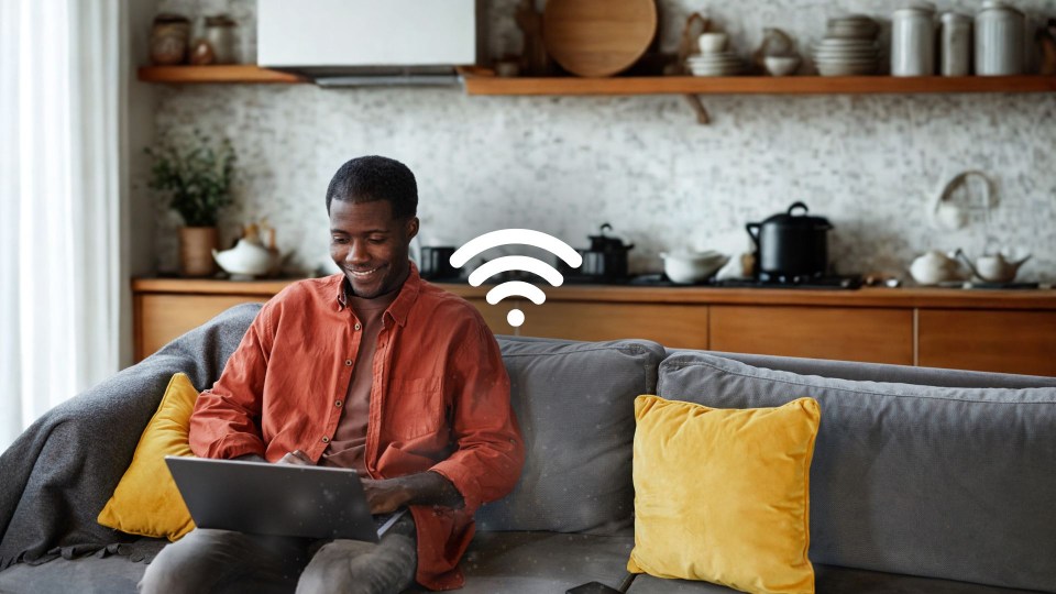 Man using a laptop on a couch with a Wi-Fi symbol.