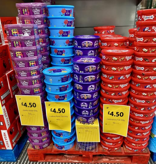 Stacks of tubs of Quality Street, Cadbury Roses, and Celebrations chocolates on sale.