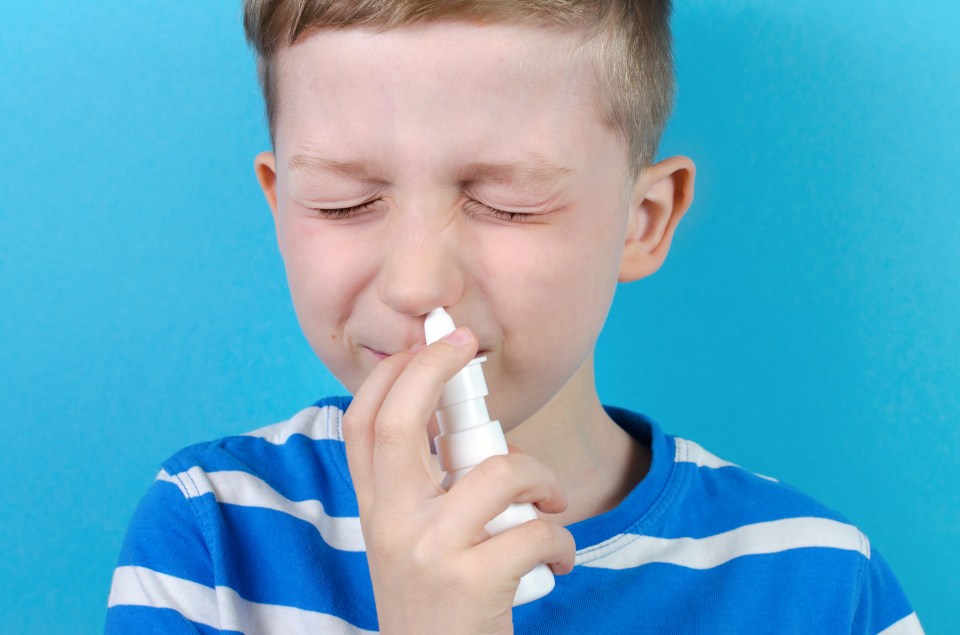 Boy with closed eyes applying nasal spray.