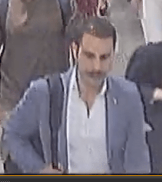 Man with mustache walking among a crowd.