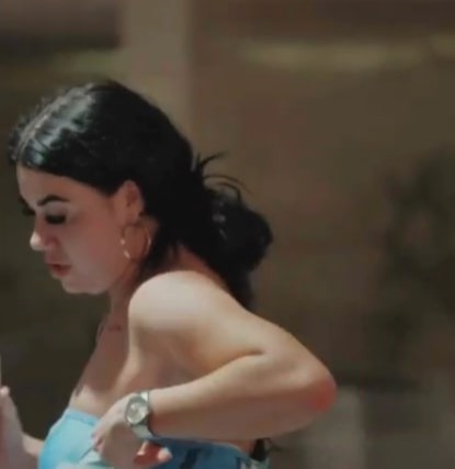 A woman in a light blue strapless top with dark hair pulled back and gold hoop earrings.