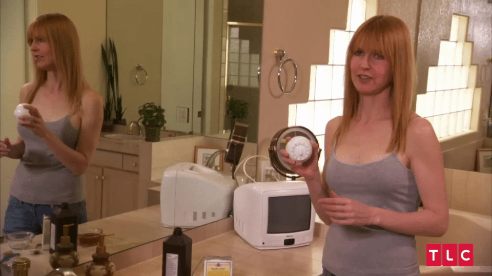 Woman in bathroom holding a round cosmetic product.