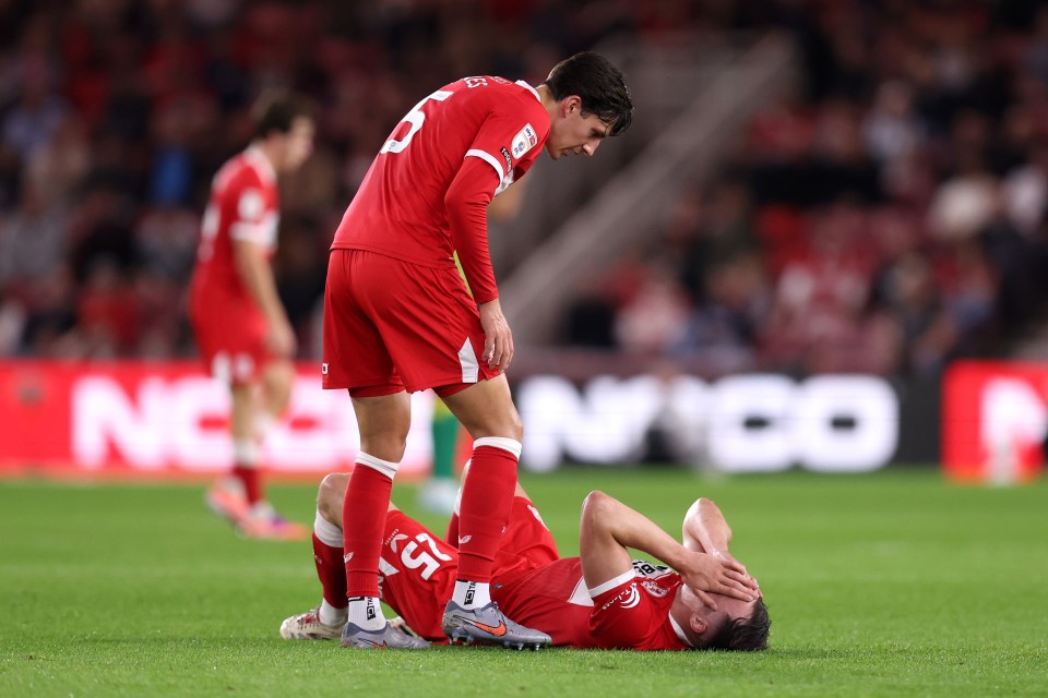George Edmundson of Middlesbrough lies on the ground with an injury, while another player stands over him.