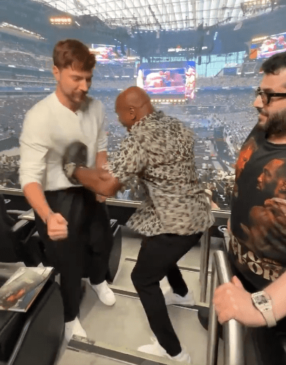 Three men in a stadium seating area, one in a leopard print shirt.