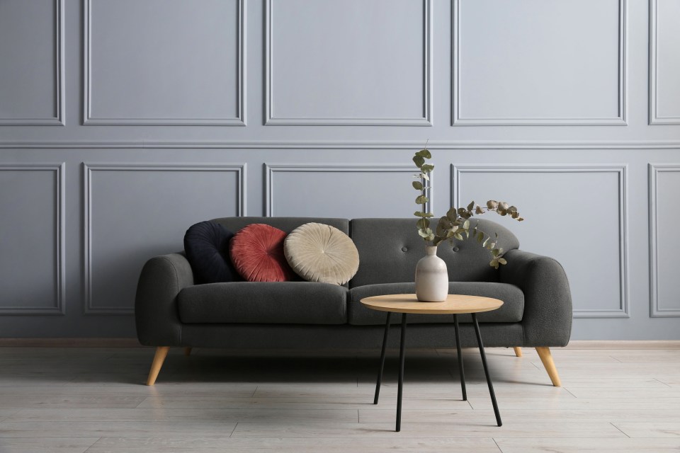 A stylish gray sofa with three round cushions and a small coffee table with eucalyptus branches in a vase.